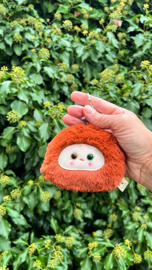 A rusty orange fluffy keychain/ bag charm with a white face and shiny eyes.