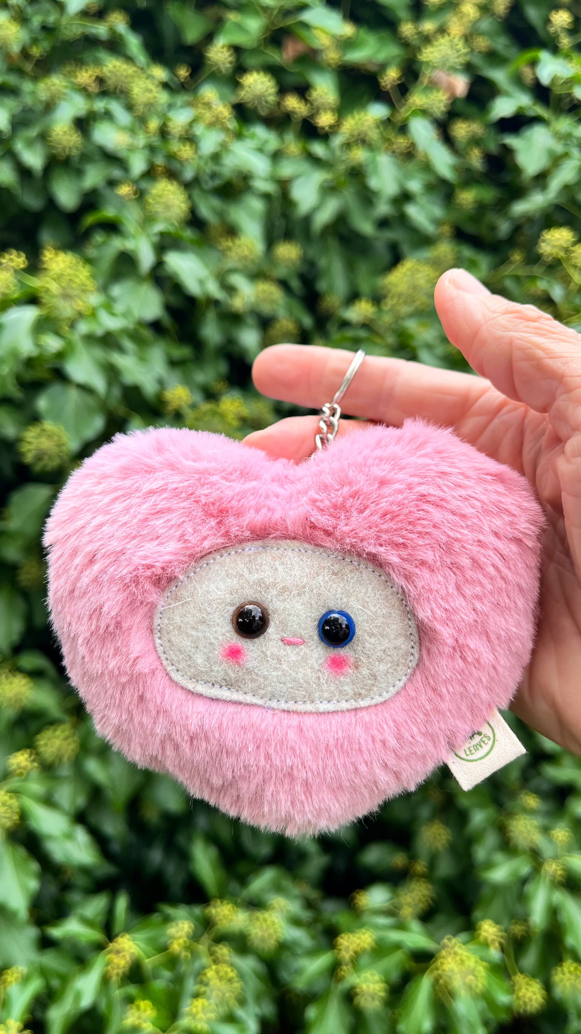A pink fluffy heart shaped keychain/ bag charm with a light grey face and shiny eyes. 