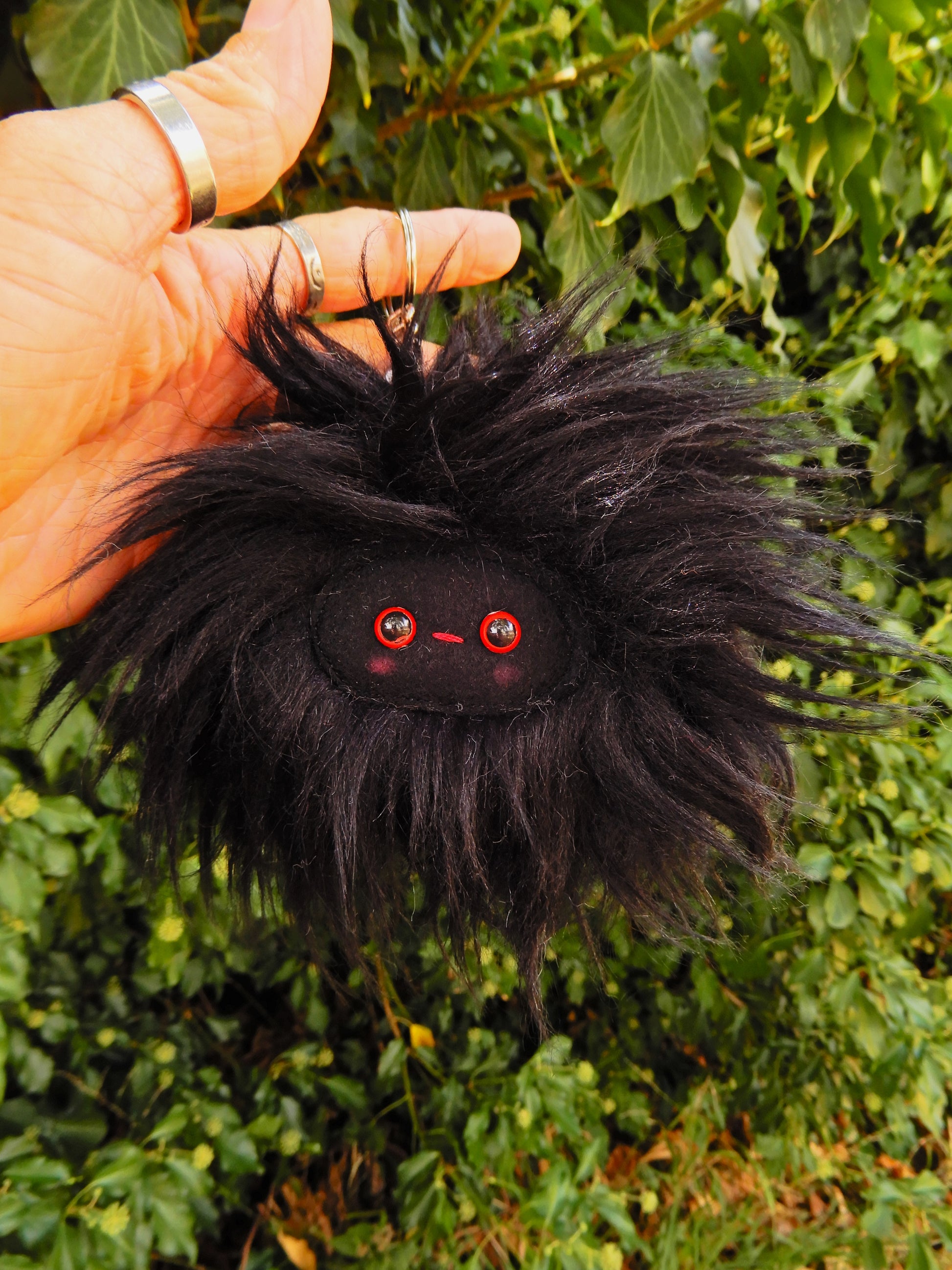 A black plush key ring/ bag charm with a black face and pink cheeks.