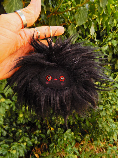 A black plush key ring/ bag charm with a black face and pink cheeks.
