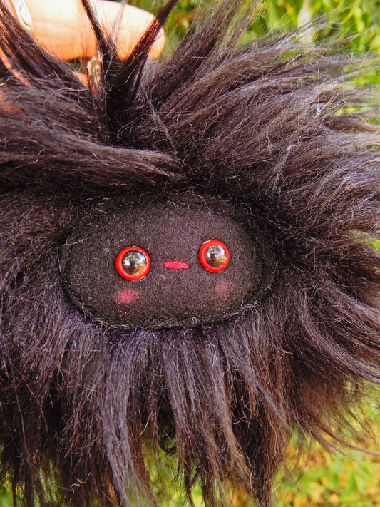 A black plush key ring/ bag charm with a black face and pink cheeks.