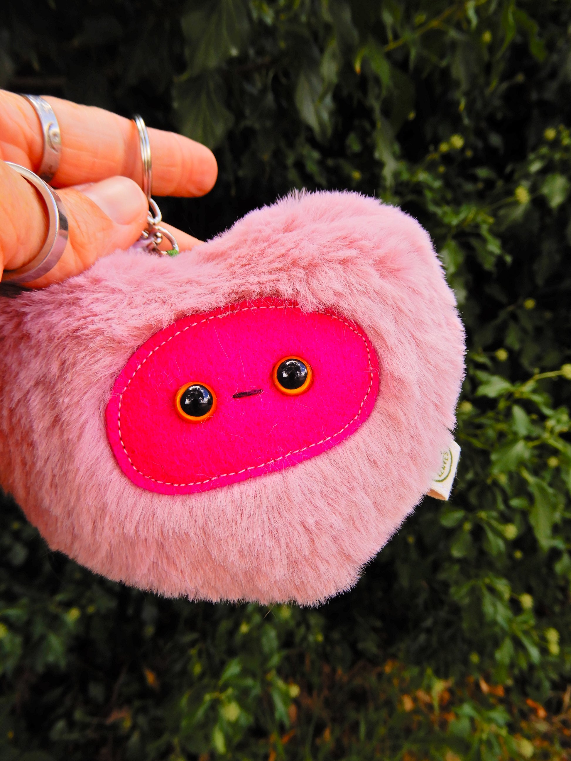 Pink heart shaped plush key chain/ bag charm with a deep pink face.
