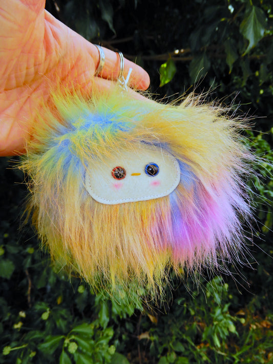 A plush rainbow keychain/ bag charm with a white face and pink cheeks.