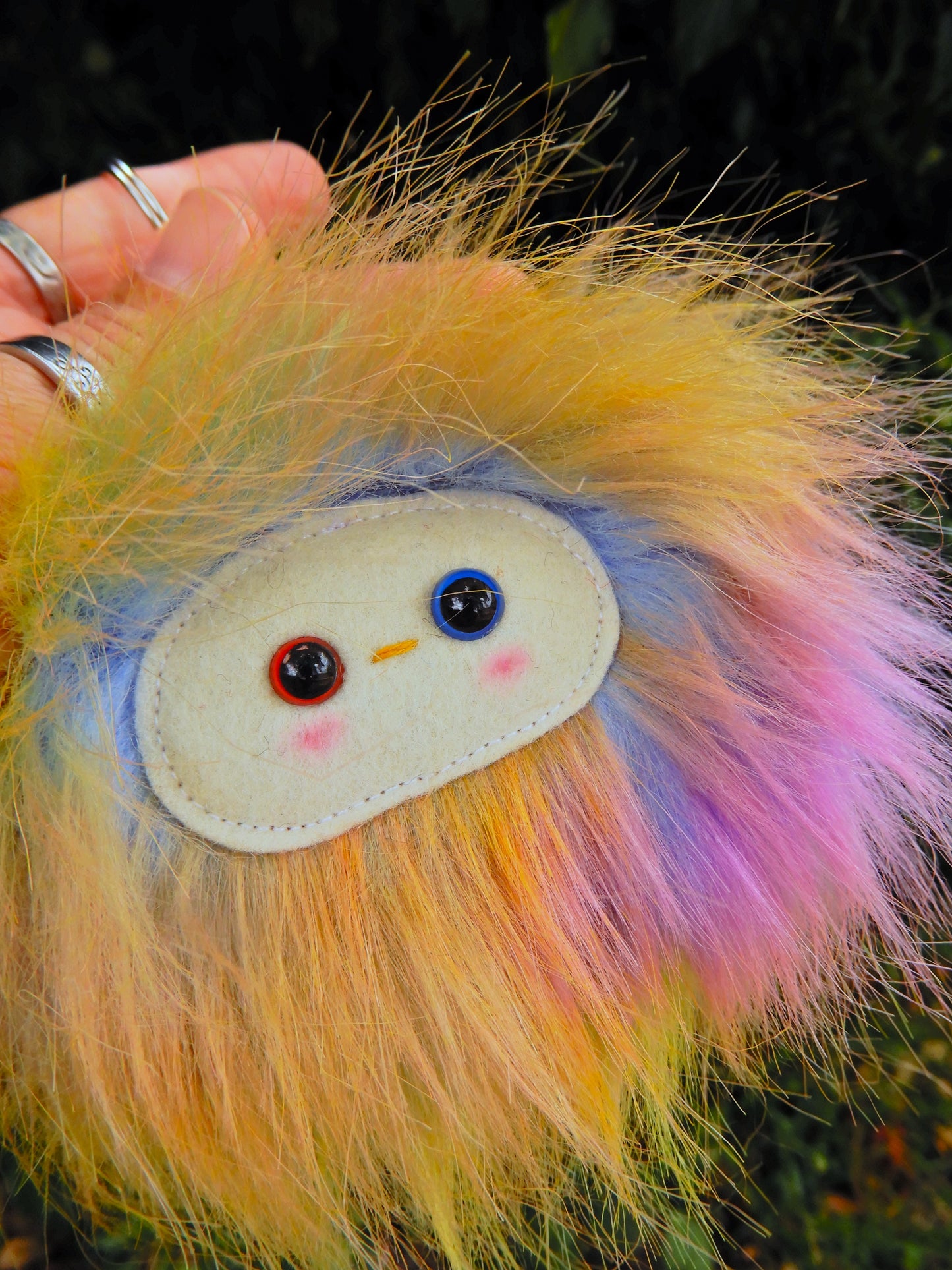 A plush rainbow keychain/ bag charm with a white face and pink cheeks.