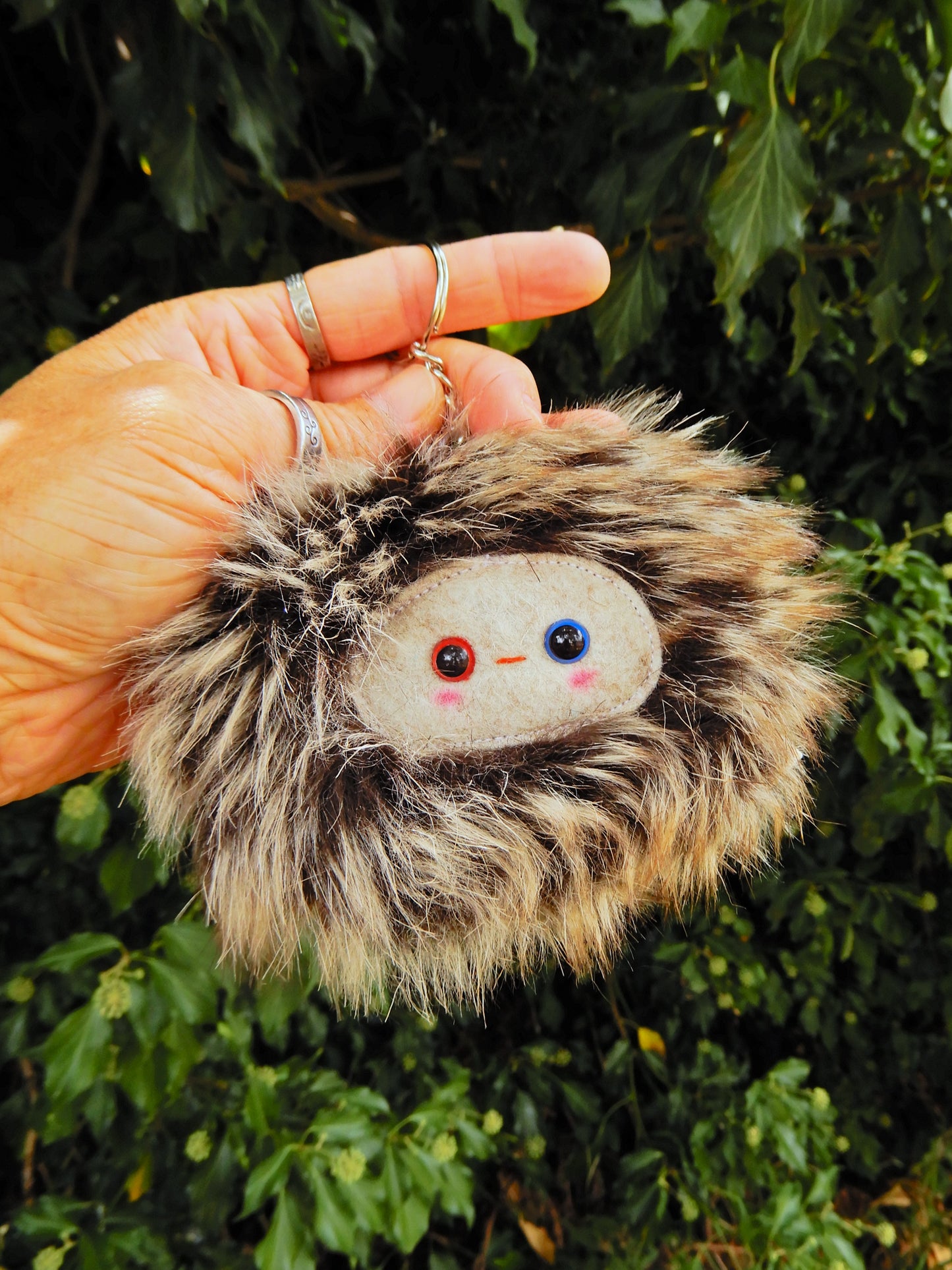 A brown fluffy plush key ring/ bag charm with a light grey face and pink cheeks.