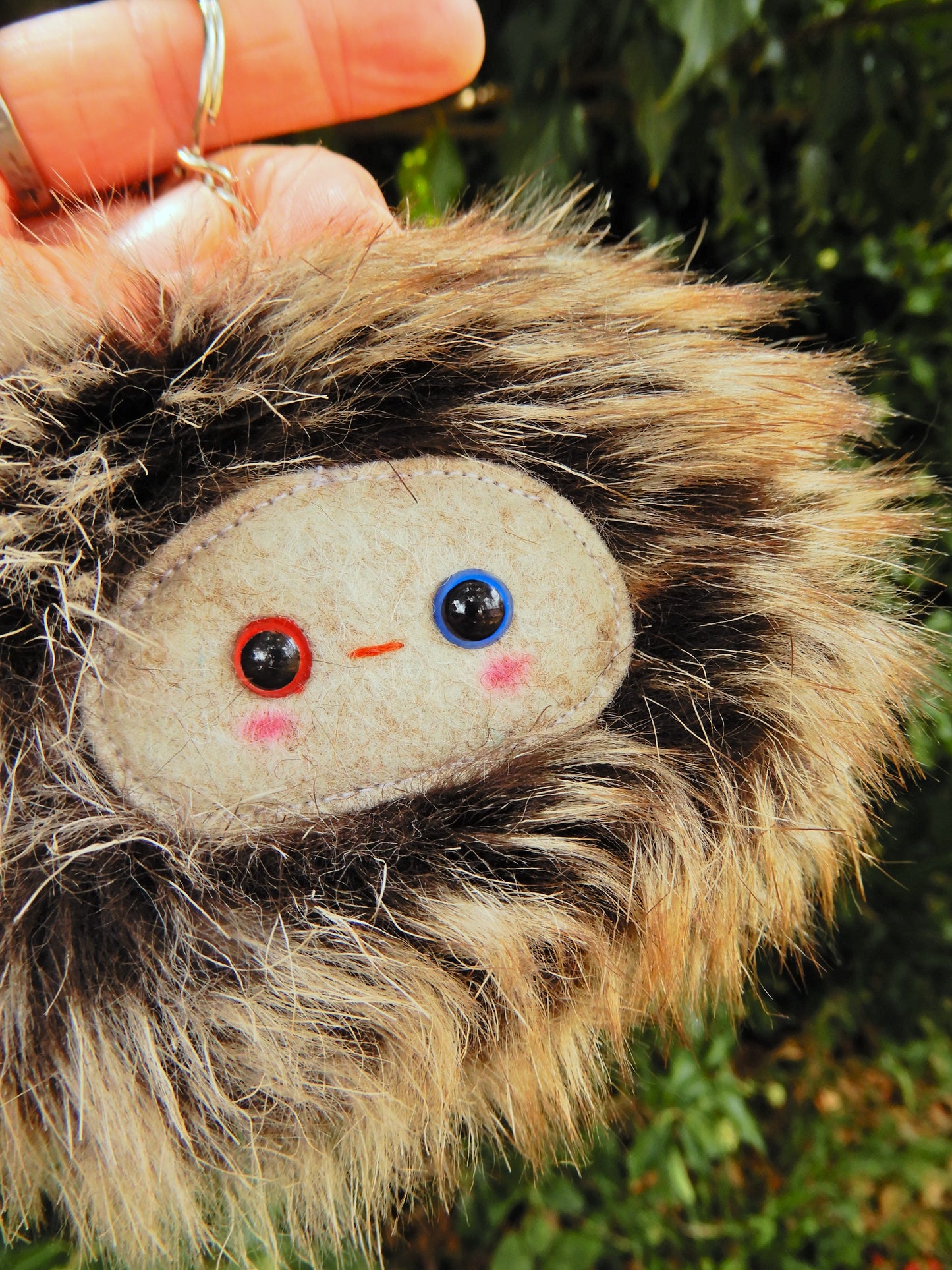A brown fluffy plush key ring/ bag charm with a light grey face and pink cheeks.