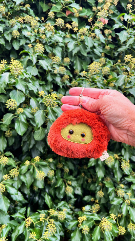 A rusty orange fluffy keychain/ bag charm with a green face and shiny eyes. 