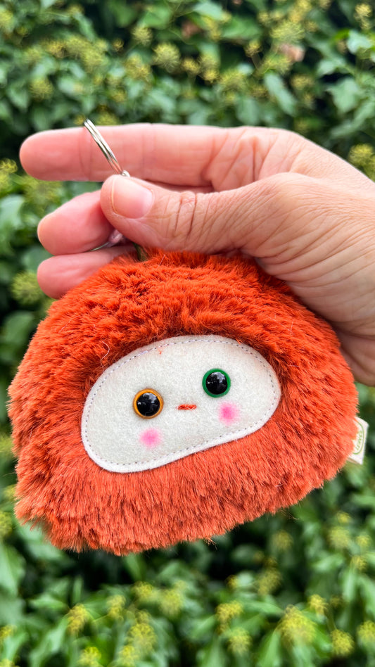 A rusty orange fluffy keychain/ bag charm with a white face and shiny eyes. 
