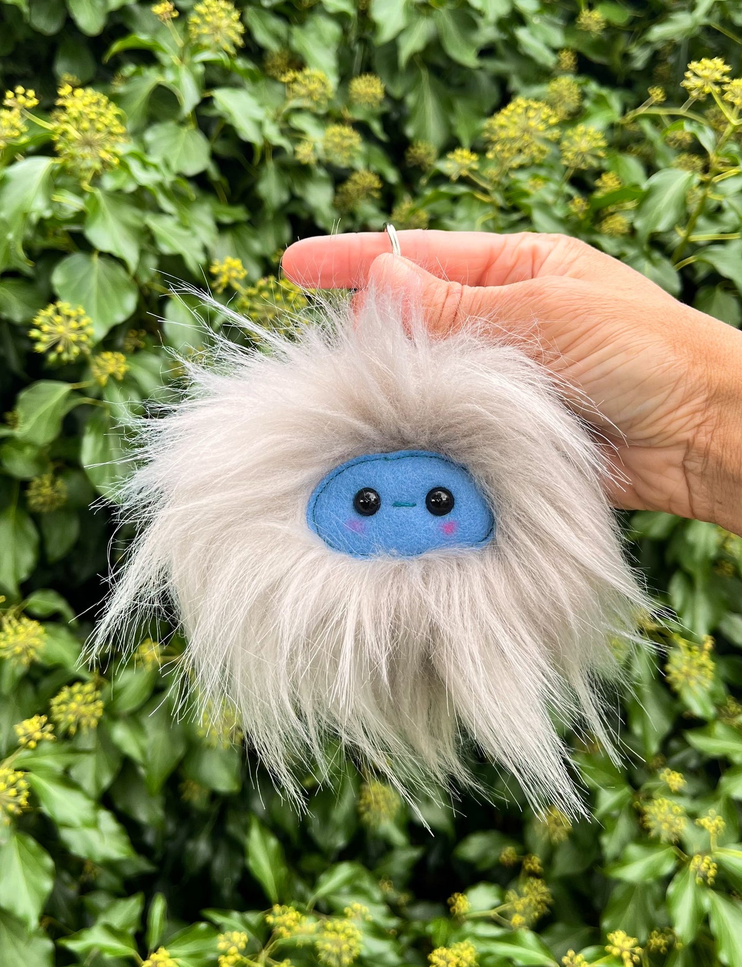 A grey extra fluffy keychain/ bag charm with a  blue face and shiny eyes. 