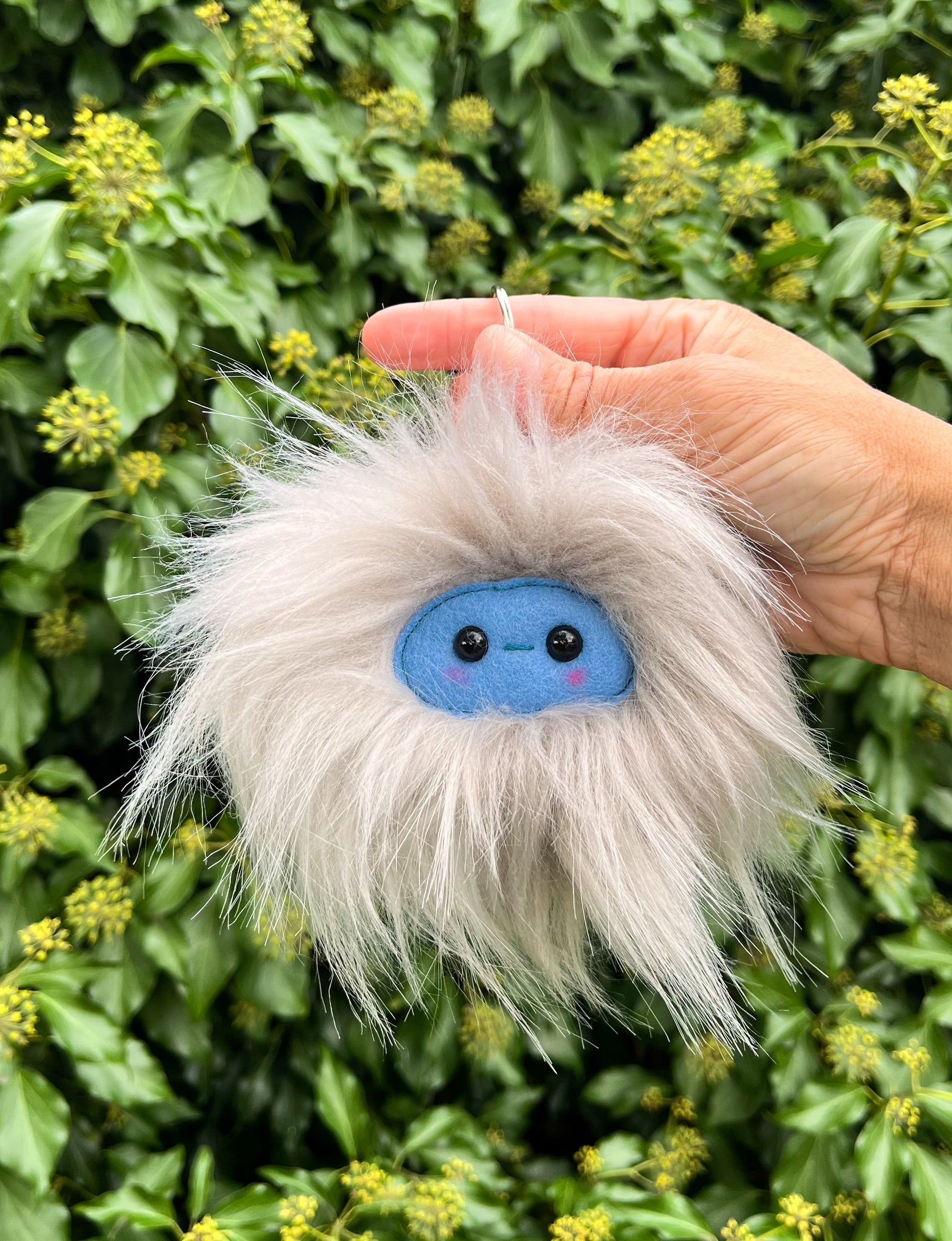 A grey extra fluffy keychain/ bag charm with a  blue face and shiny eyes. 