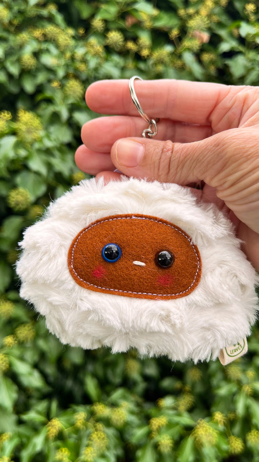 A white fluffy keychain/ bag charm with a brown face and shiny eyes. 