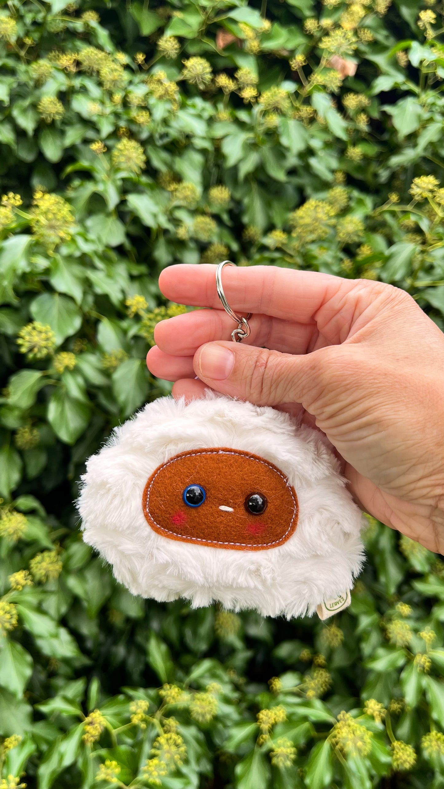 A white fluffy keychain/ bag charm with a brown face and shiny eyes. 
